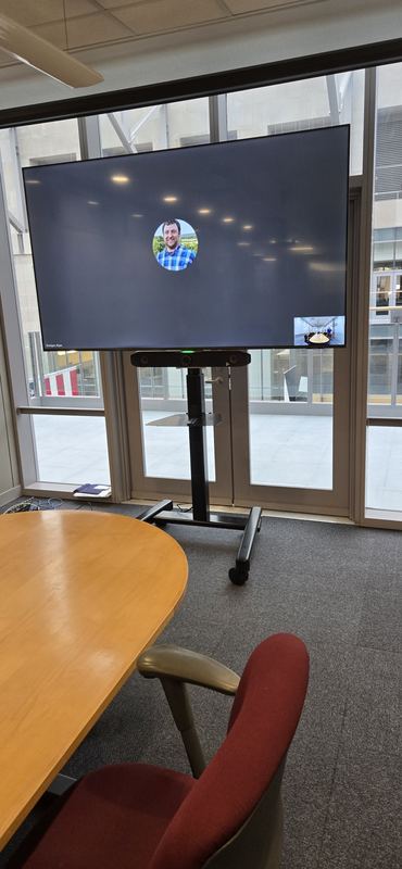 Mobile display, glazed bay — Display on a mobile lift base in a daylight-heavy meeting bay.