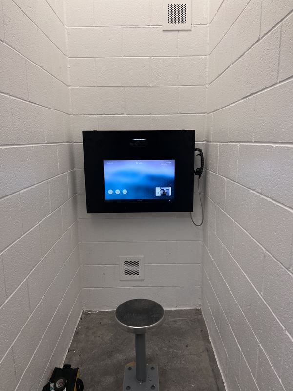 Video visitation station — Inmate-side visitation terminal set into a block-wall alcove, with handset and fixed seating.