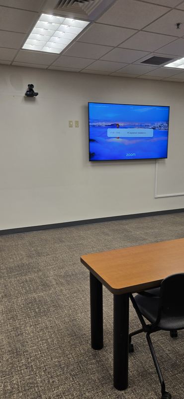 Meeting room — Compact room with display and ceiling-mounted camera on the opposing wall.